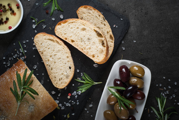 Italian ciabatta bread  on black slate with herbs and olives. - Zdjęcie, obraz