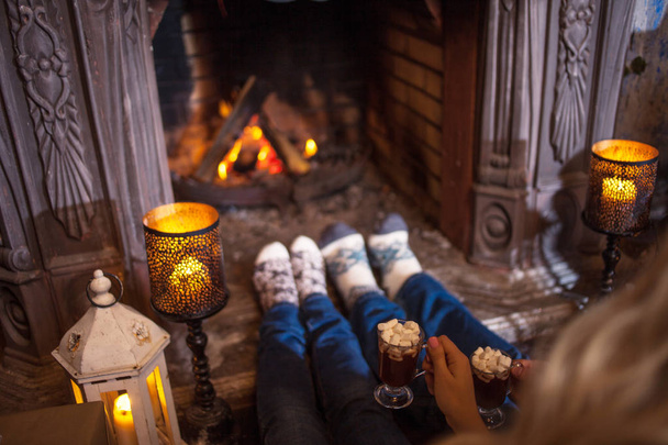 Paar ontspannen thuis chocolademelk drinken. Voeten in sokken van wol in de buurt van open haard. Concept van winter vakantie - Foto, afbeelding