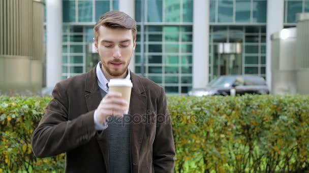 Attractive man drinking coffee or tea from paper cup, looking at camera, smiling - Video