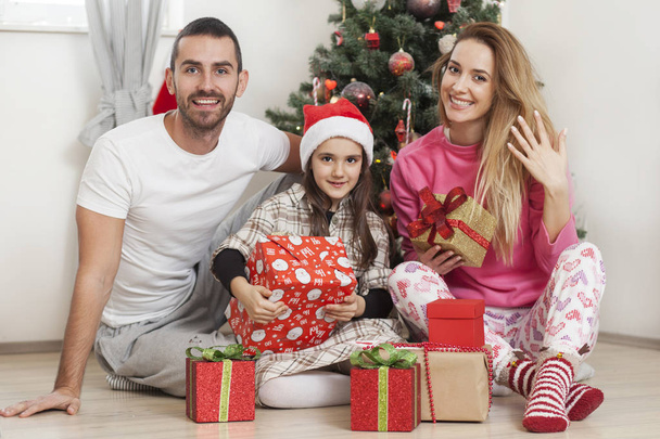 family in front of Christmas tree opening presents - Foto, Imagen