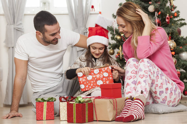 family in front of Christmas tree opening presents - 写真・画像