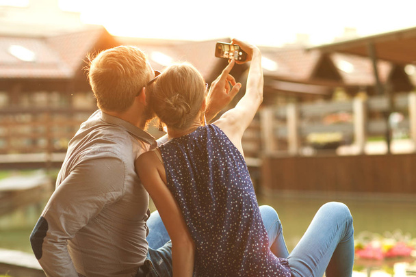 paar in liefde zit in het park bij zonsondergang maakt de selfie - Foto, afbeelding