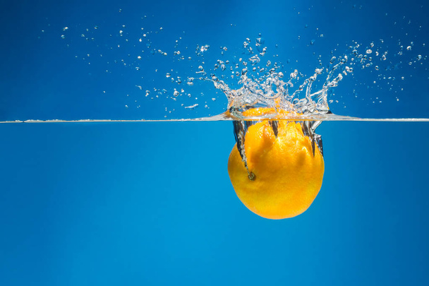Tangerine in water with splashes on a blue background - Foto, imagen