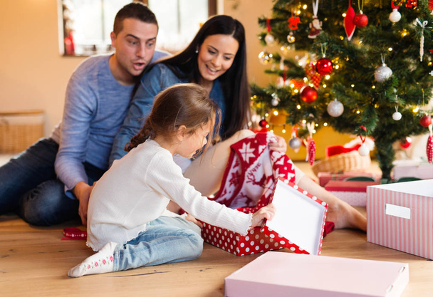 Familia joven con hija en el árbol de Navidad en casa
. - Foto, Imagen