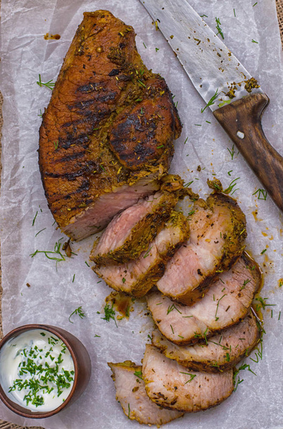 Pork steak cooked on the grill, marinated in herbs and rosemary, served  a table with tzatziki sauce. Background paper for baking. Top view. Close-up - Photo, Image