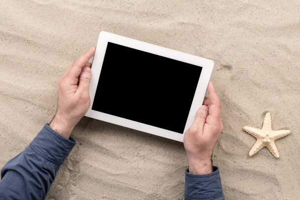 Man holding tablet with blank screen lying on the beach - Photo, image