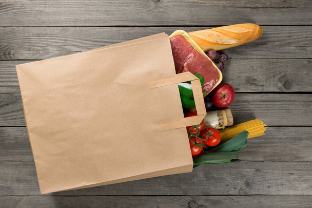 Paper bag full of different food on wooden background - Фото, зображення