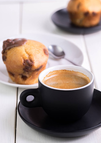 Πρωινός καφές στο φλιτζάνι μαύρο σε άσπρο φόντο φυσικά με muffin πίσω από. - Φωτογραφία, εικόνα