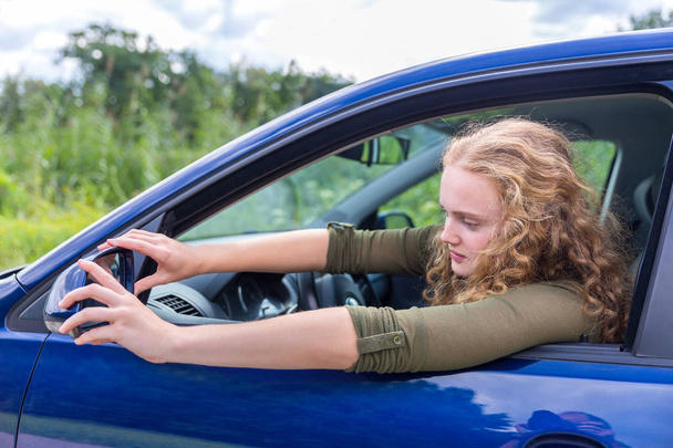 Mujer caucásica ajustando espejo lateral del coche
 - Foto, Imagen
