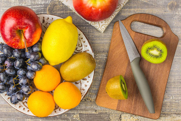 Apple Orange, lemon, fruit, KIWI, the plate and wooden Board. Knife grapes background on a  table. - Fotografie, Obrázek