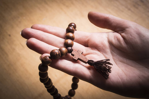 Rosary and cross in female hands on a wooden background.  - Photo, Image