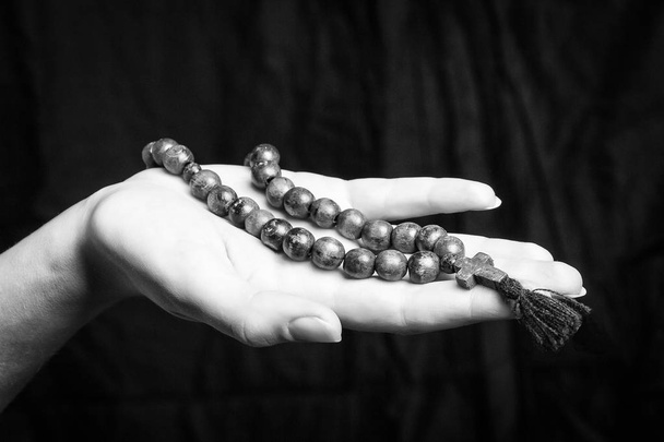 Rosary and cross in female hands on a dark background. Black and white photo. - Photo, Image