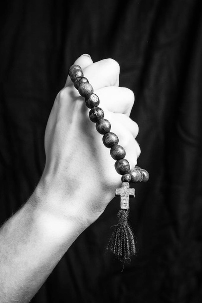 Ροζάριο και σταυρό στα γυναικεία χέρια σε σκούρο φόντο. Μαύρο και άσπρο φωτογραφία. - Φωτογραφία, εικόνα