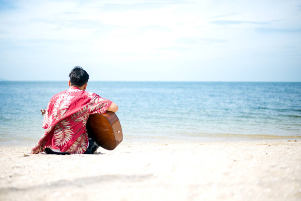 Pohledný muž hraje klasická kytara sedí na pláži dovolenou - Fotografie, Obrázek