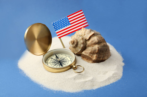 USA flag, compass and shell in sand on blue background. Columbus Day concept - Foto, afbeelding