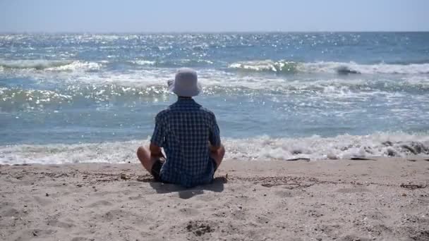 Człowiek siedzi na brzegu morza - Materiał filmowy, wideo