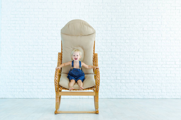 Little girl rides a rocking chair on the background of a white brick wall. - Zdjęcie, obraz