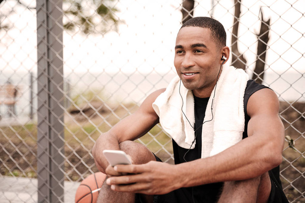 Basketball player sitting in park with phone and listen music - Foto, imagen