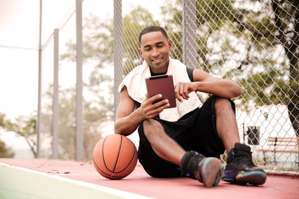 Happy african basketball player sitting in park and using tablet - Photo, image