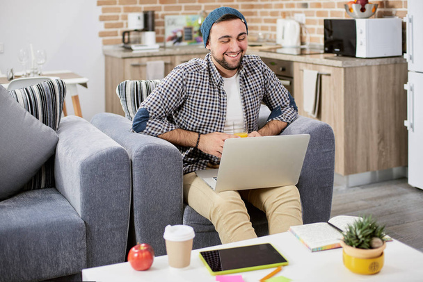 Portret van gelukkige jonge Glimlachende man, student of freelancer zakenman, werkt op zijn laptop gezellige moderne thuis in loft-stijl - Foto, afbeelding