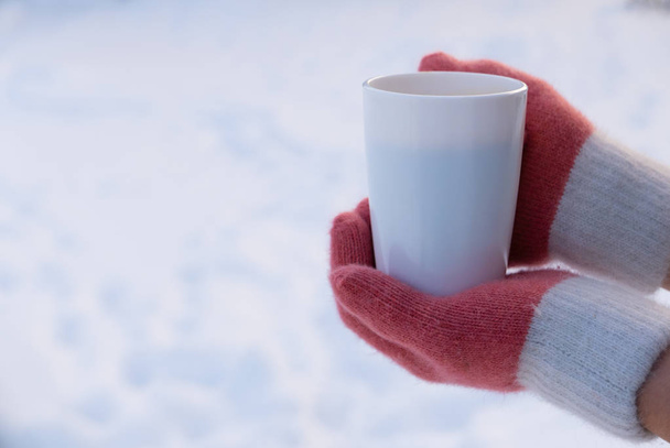 Mujer con guantes sosteniendo taza blanca de té o café en la nieve
 - Foto, Imagen