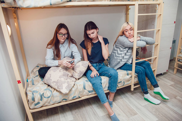 Mooie meisjes zittend op een bed in hostel praten en het gebruik van smartphone. - Foto, afbeelding