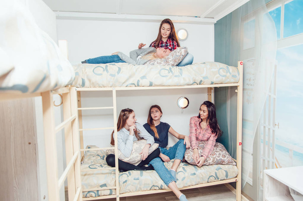 Beautiful girls sitting on a bed in hostel talk and have fun. - Valokuva, kuva