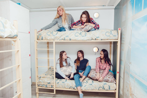 Beautiful girls sitting on a bed in hostel talk and have fun. - Fotó, kép