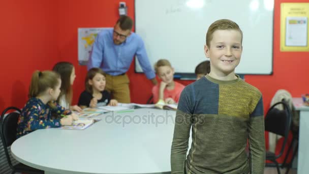 Mały uczeń gestykulacji kciuk w górę trzymając książek z kolegami w tle - Materiał filmowy, wideo