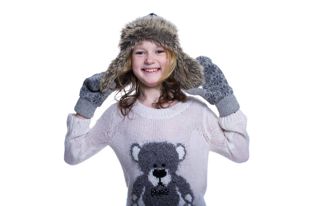 Happy cute kid posing in the studio. Wearing winter clothes. Knitted woolen sweater and mittens. Ear flaps fur cap. Isolated on white background. - Photo, Image