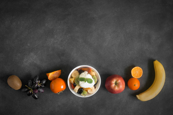 Bowl of healthy fresh fruit salad with mint on black chalkboard - Foto, Bild