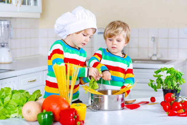 Два маленьких мальчика готовят макароны с овощами
 - Фото, изображение