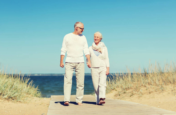 happy senior couple holding hands on summer beach - 写真・画像