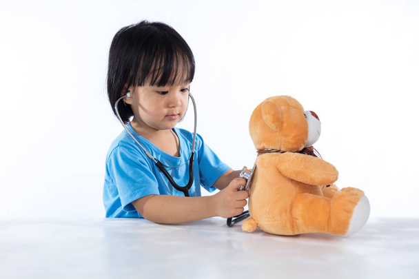 asiatische chinesische kleine Arzt Mädchen untersuchen Teddybär  - Foto, Bild