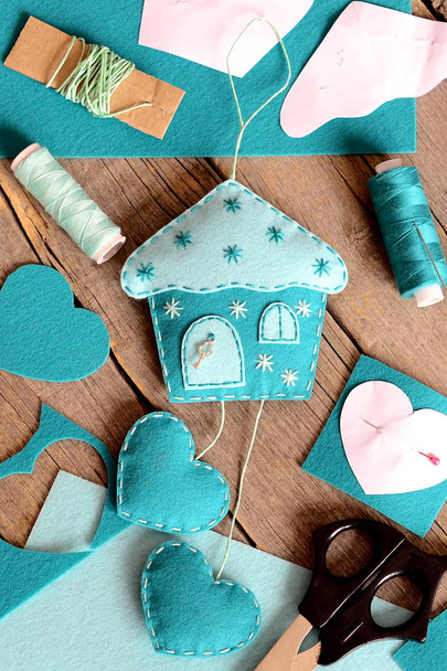 Felt house with hearts ornament, tools and materials for hand making felt crafts, paper patterns on wooden table. Hanging wall decor in form of house with hearts. Kids sewing workplace. Rustic style  - Fotoğraf, Görsel