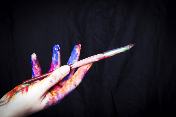 Руки художника в яркой цветной краске с кистью на черном фоне
. - Фото, изображение
