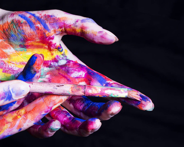 Руки художника в яскравій кольоровій фарбі з пензлем на чорному тлі
. - Фото, зображення