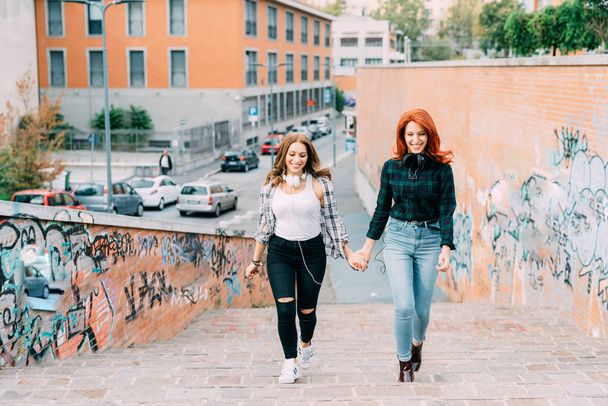 mujeres amigas caminando de la mano con auriculares
 - Foto, Imagen