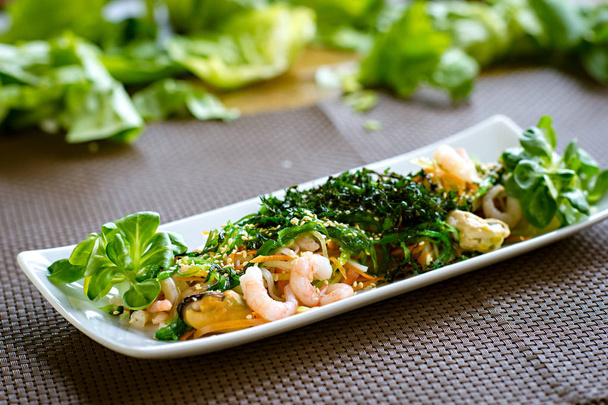 Ensalada japonesa saludable con mariscos, algas marinas y semillas de sésamo en placa blanca
 - Foto, imagen