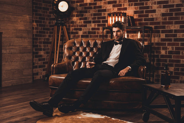 Young man in suit resting on sofa with glass of brendy after wor - Foto, Imagem