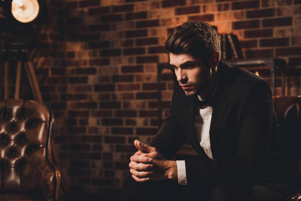 Young minded businessman in black suit sitting on leather sofa - Photo, image