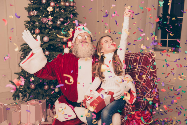 Party with confetti. Little happy girl sitting on lap of santa w - Photo, Image
