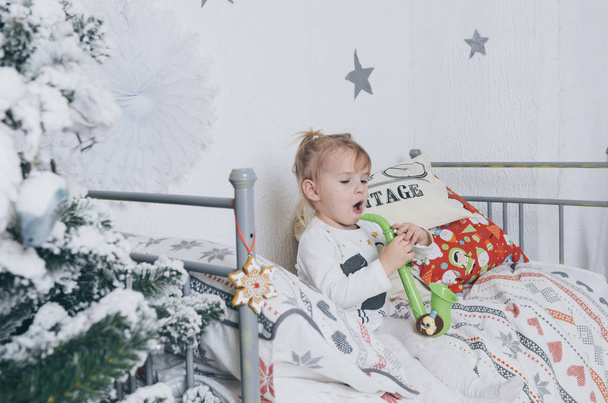 Красивая маленькая девочка развлекается на своей плохой рядом с рождественской елкой в комнате. Играть на саксофоне и танцевать
  - Фото, изображение