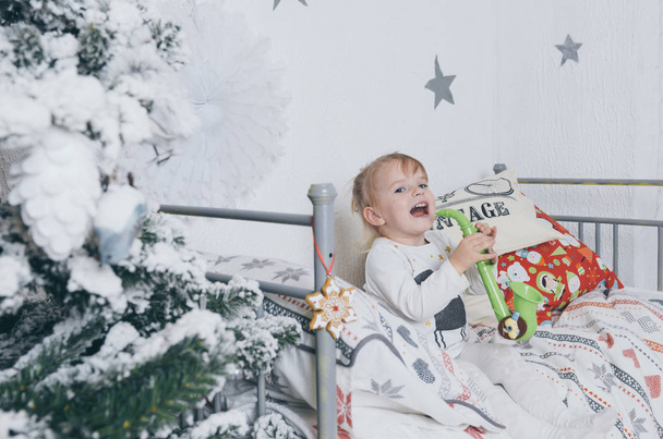 schönes kleines Mädchen hat Spaß auf ihrem Bett in der Nähe des Weihnachtsbaums  - Foto, Bild