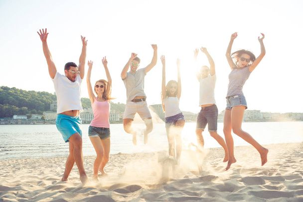 Young friends enjoying  beach party and jumping on summer sunset - Fotoğraf, Görsel