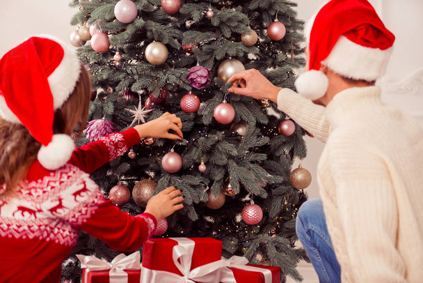 Pareja enamorada usando sombreros de Papá Noel y decorando el árbol de Navidad
  - Foto, imagen