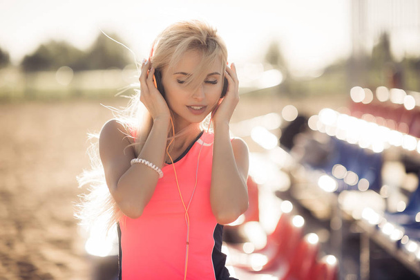 Porträt eines sportlichen pubertierenden Mädchens, das sich vom Sport erholt, Musik mit Kopfhörern hört und im Freien lächelt. Fitness und Sport Lifestyle, sonnige Außenfassade. - Foto, Bild