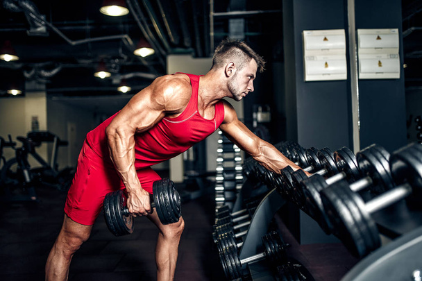 Determined bodybuilder lifting heavy black dumbbells at the gym. - Φωτογραφία, εικόνα