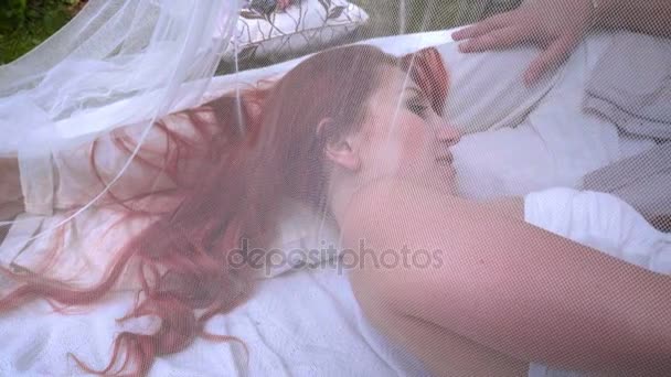 Dating couple lying on white cloth behinde transparent fabric in park - Кадри, відео