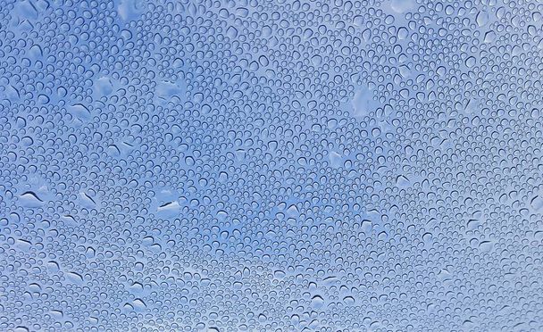 Вода падає на скло з розмитим блакитним фоном неба
 - Фото, зображення
